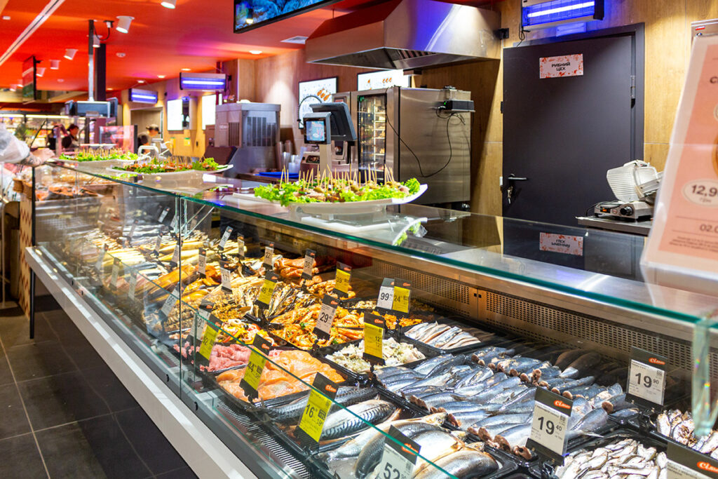 Grocery store fish counter with a glass display case filled with fresh seafood and price tags on each item.—informative image of a seafood department